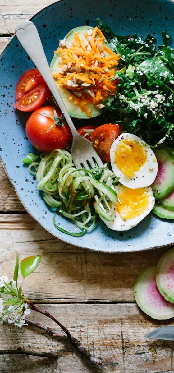 A bowl of greens, tomato, courgette and soft-boiled egg on a wooden table